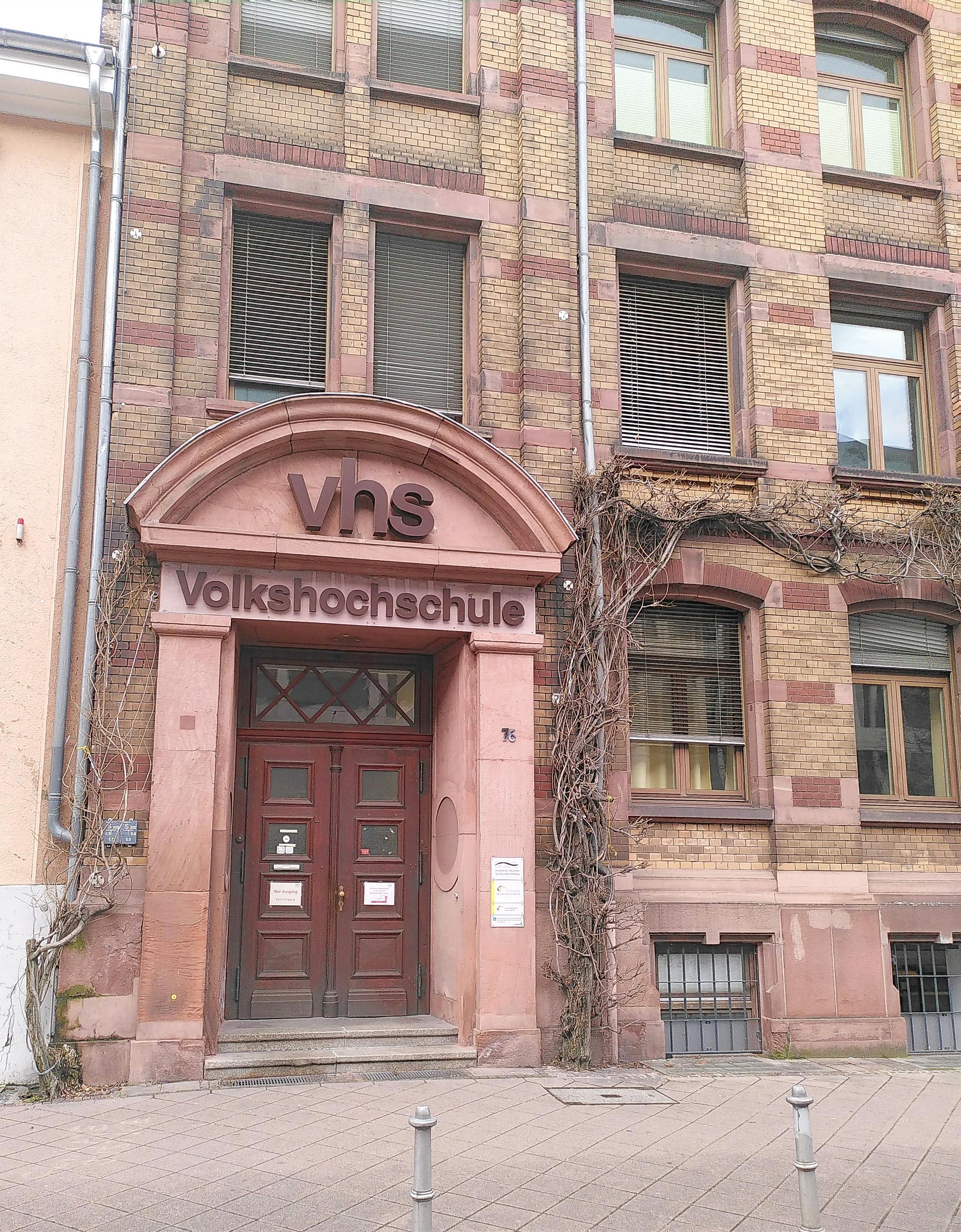 Eingangstüre in einem Backsteingebäude, Rundbogen. Darin steht VHS Volkshochschule.